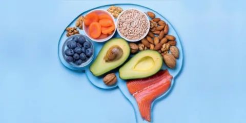 Various brain-healthy foods—including salmon, blueberries, almonds, walnuts, sunflower seeds, and avocado—arranged in the shape of a human brain on a blue background.