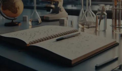An open notebook with a pen lying on it, set in a dimly lit science or study environment, symbolizing the practice of journaling and reflection.